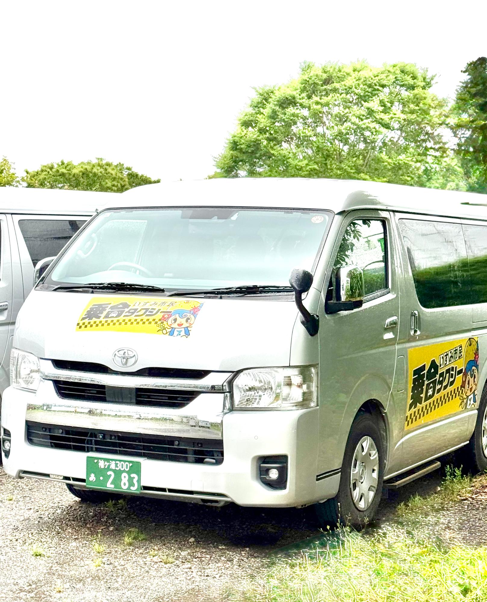 車体の左斜め前から撮影し、フロントガラスの下に黄色の背景に黒字で「いすみ市民乗合タクシー」のロゴがあり、同じロゴが側面中央にもある写真