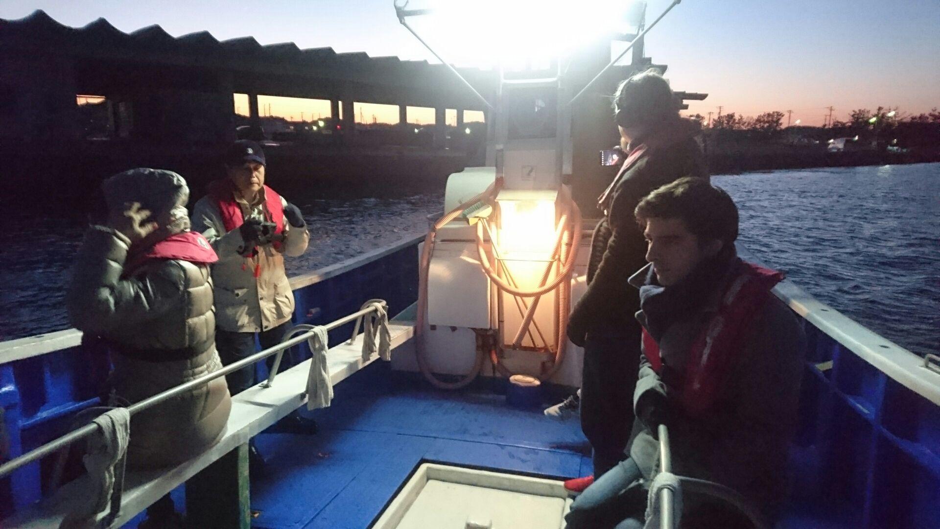 美しい夕焼けをバックに明るい船内灯に照らし出されながら、ライフジャケットを着込み漁船に乗り込んでいる留学生の皆さんの写真