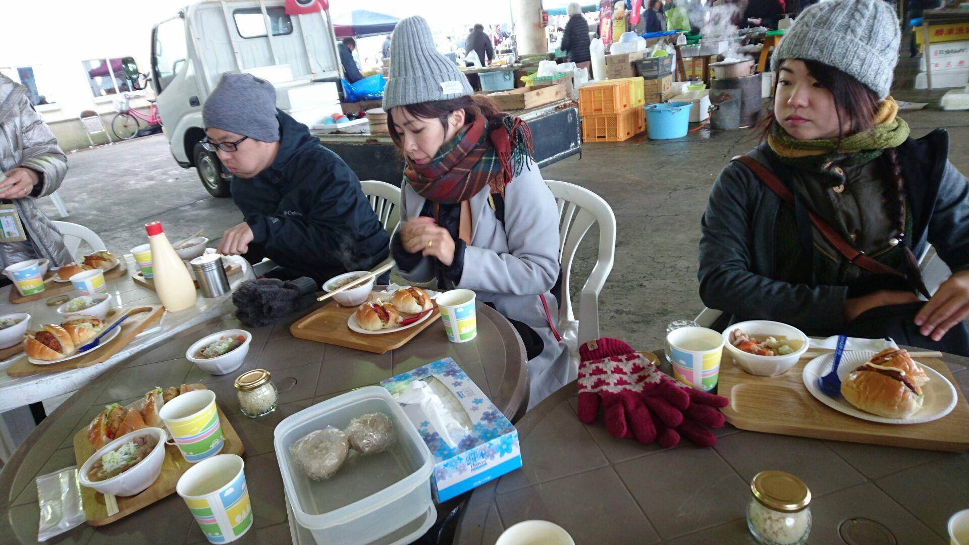 毛糸のニット帽と暖かそうなアウターを着込んだお客さん数名が、食事スペースのテーブルに並んでパンとスープの食事をとっている様子の写真
