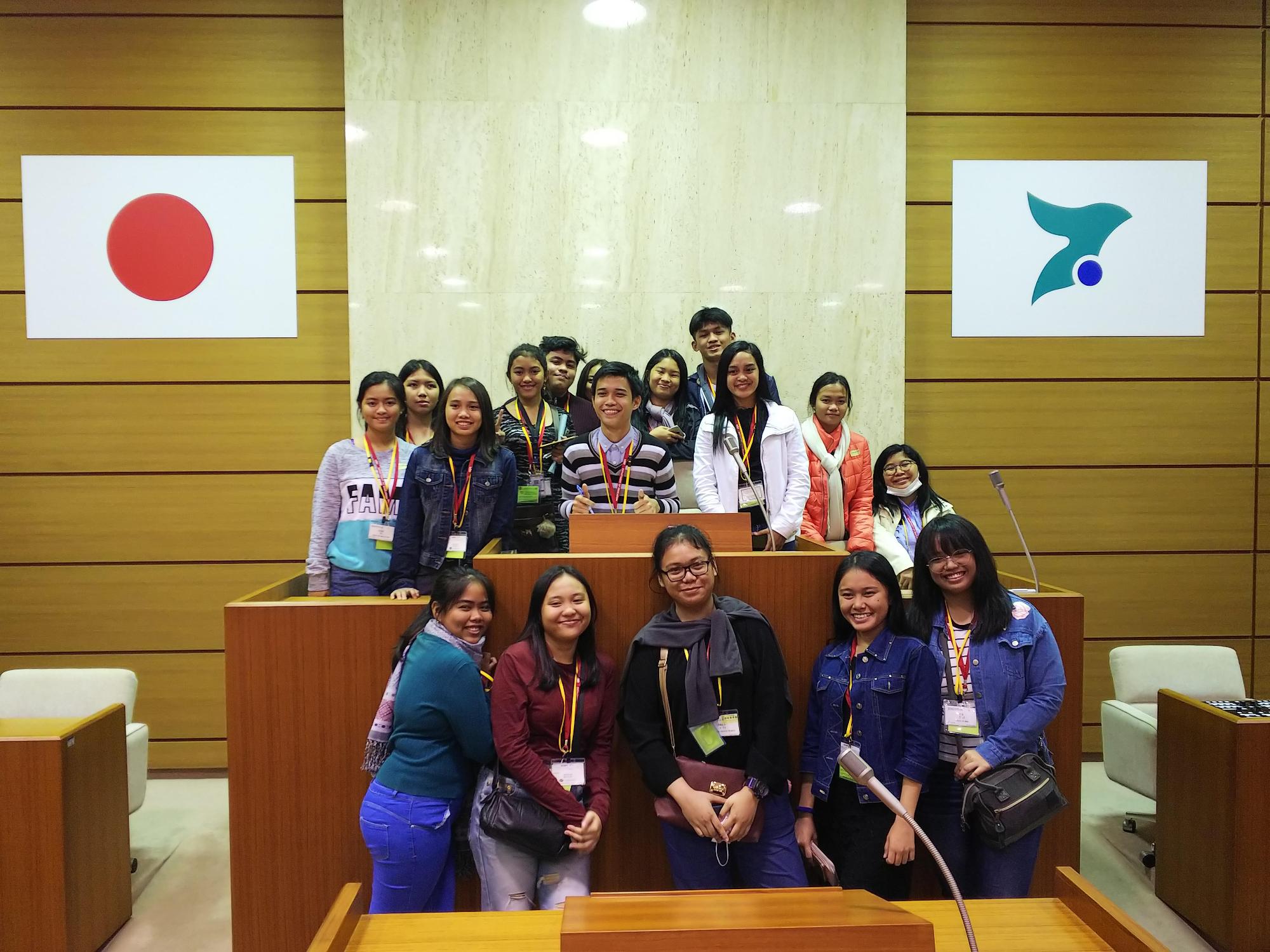 日本の国旗といすみ市のシンボルマークが掛けられた会議室の壇上で整列して笑顔で写真に映るフィリピンの中高生の皆さんの写真