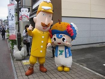 茶色い軍靴に黄色い制帽と軍服を着て茶色い口ひげを付けた新潟県のゆるキャラ「レルヒさん」の着ぐるみと並んで、可愛くポーズをとる「いすみん」の写真