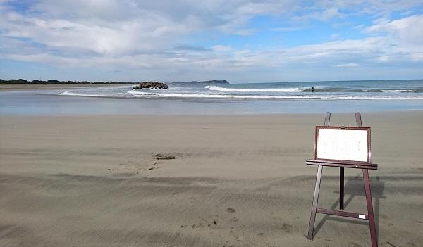 青空の下、白波が立つ広い砂浜に、イーゼルに飾られた賞状が置かれている写真